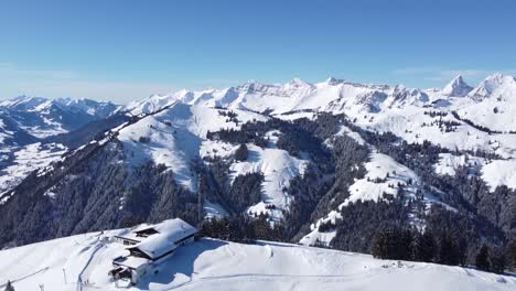una cabaña de montaña en la nieve frente a un montón de bosque y los impresionantes alpes suizos