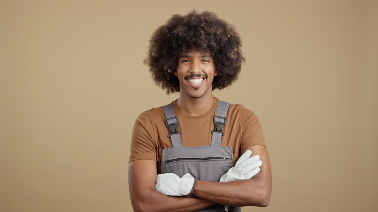 Een lachende man in werkoveral en handschoenen met een afro