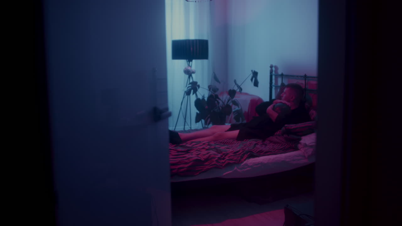 Man relaxing in a purple and pink lit bedroom