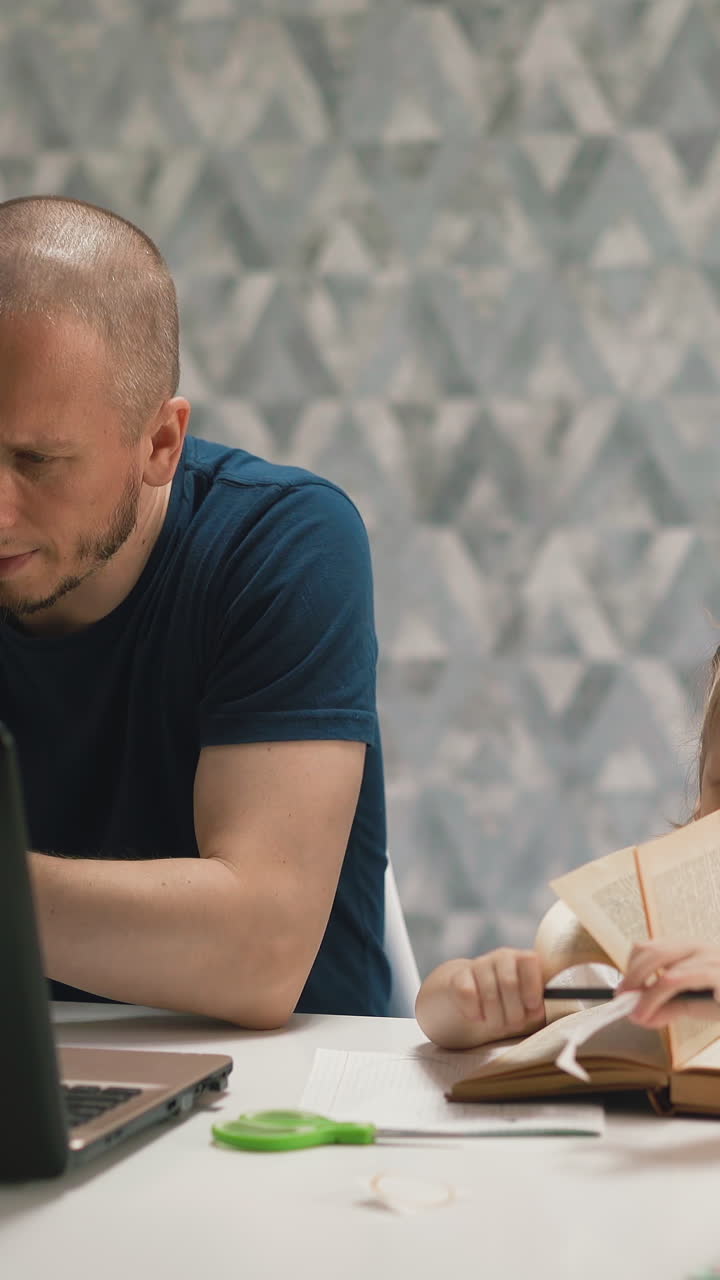 young daughter do homework, sits at table with book, on distance learning, dad sits next, works at computer and talks on phone, say girl not to interfere and not to distract