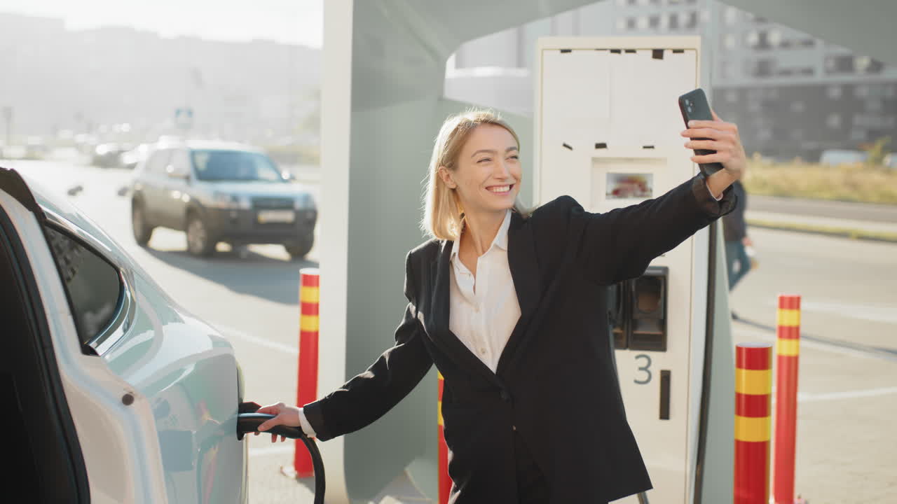 una mujer de negocios se toma una selfie mientras carga un vehículo eléctrico.