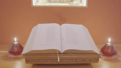 Old-book-open-at-the-wooden-table-with-two-red-candles---slow-dolly-shot