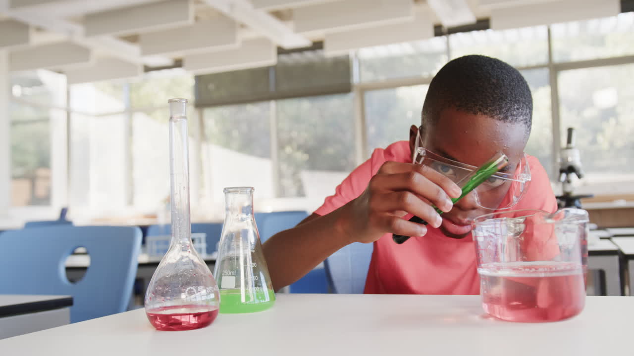 Conducting science experiment, boy in school lab examining test tube with goggles