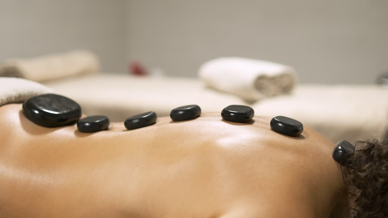En kvinde modtager afslappende hot stone rygmassage på et massagebord.