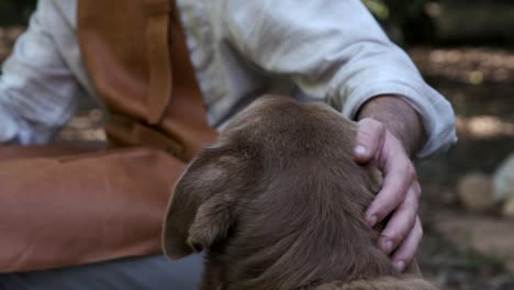 man in a leather apron pets his brown labrador dog