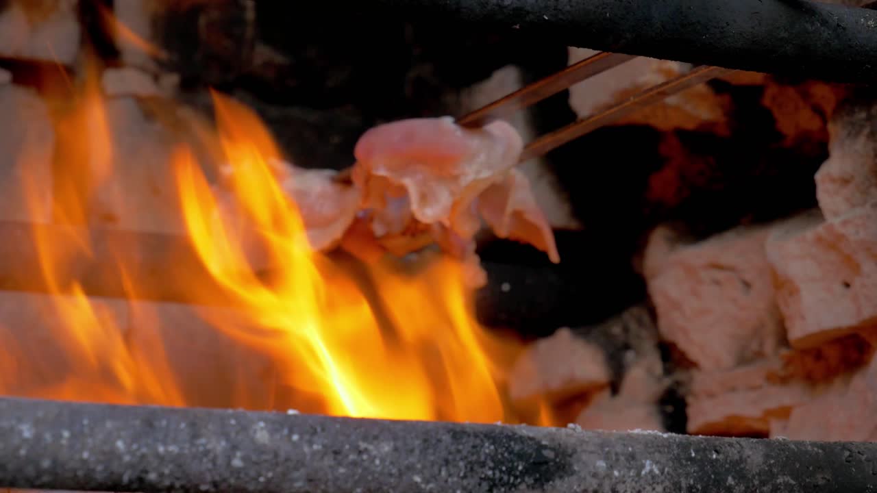 거대한 불에 베이컨을 손으로 들고 요리하는 동안 셰프가 바삭바삭한 맛을 위해 반대편에서 베이컨을 굽습니다
