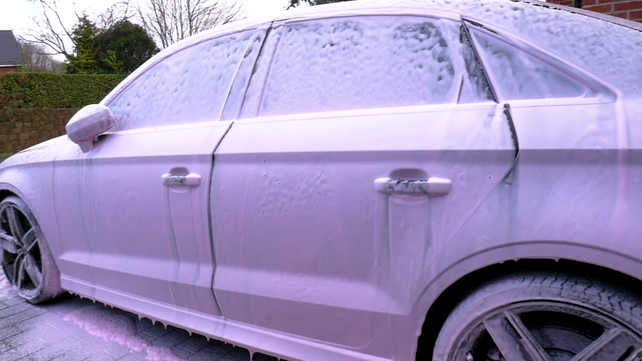 Side View of a Black Car Covered In Pink Snow Foam