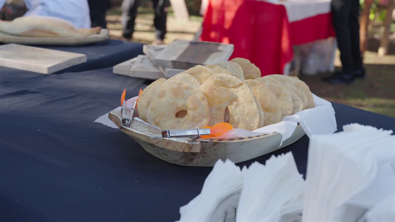 Traditionella argentinska tortas fritas är arrangerade på en bricka fodrad med servetter vid ett utomhusevenemang, fångade i slow motion för att framhäva textur och gyllene färg under mjukt naturligt dagsljus