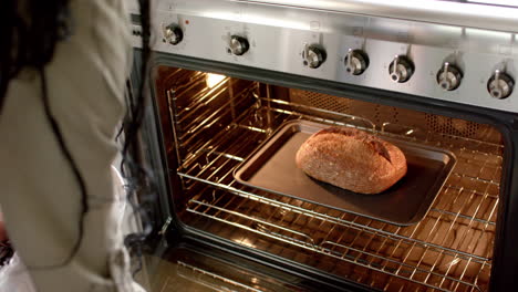 An-African-American-woman-wearing-watch,-taking-out-fresh-bread-from-oven