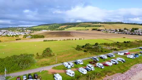 aerial drone footage glides over rural caravan campsite, grassy fields, rolling hills, and parked vehicles