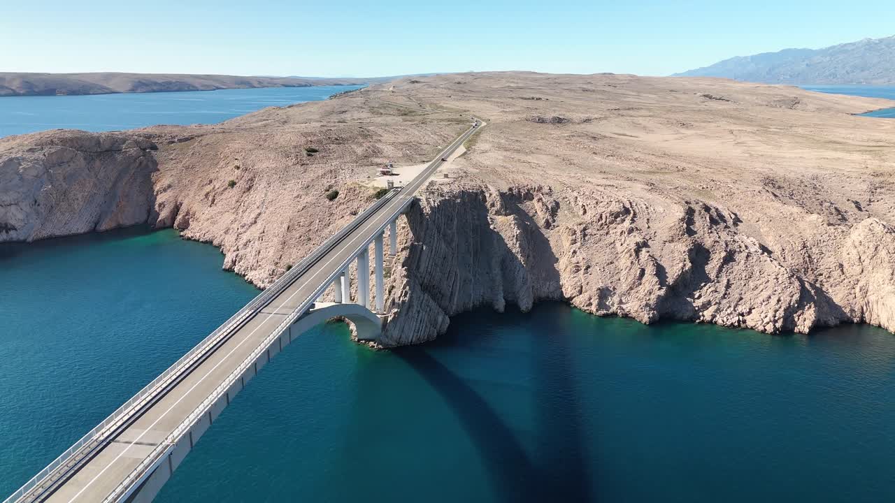 Drone aerial view of Pag Bridge linking the Croatian mainland with Pag Island. Blue Adriatic Sea contrasts with the island’s white rocky landscape in summer