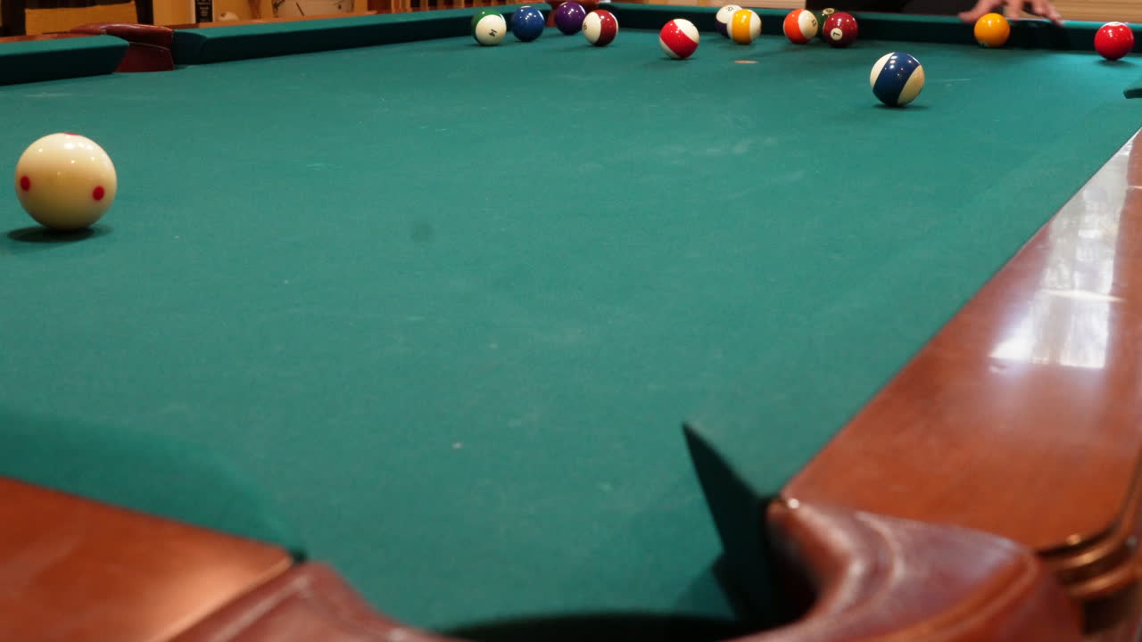 Person Racks 8 Ball Pool Game on the Spot Gathering Solid and Stripped Billiard Balls on Table with Green Felt and Tightening Rack with Hands before Lifting Wooden Triangle, low angle no faces