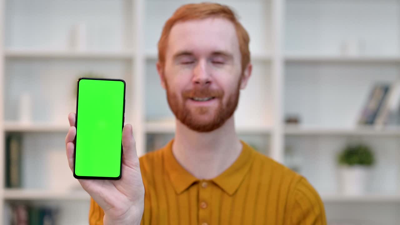 retrato de un hombre pelirrojo mostrando un teléfono inteligente con pantalla cromada