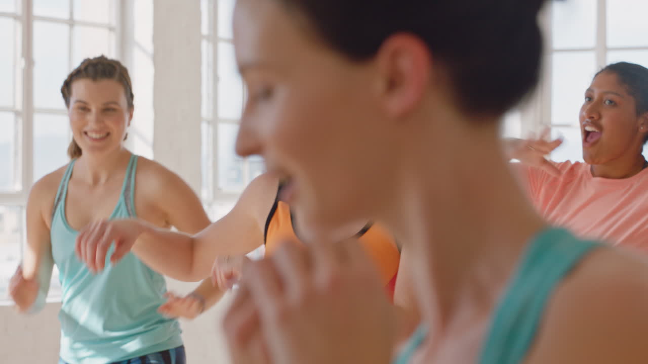아름다운 백인 여성 춤추는 건강한 사람들 그룹이 활기찬 피트니스 스튜디오에서 즐겁게 안무 댄스 동작을 연습하는 것을 즐기고 있습니다.