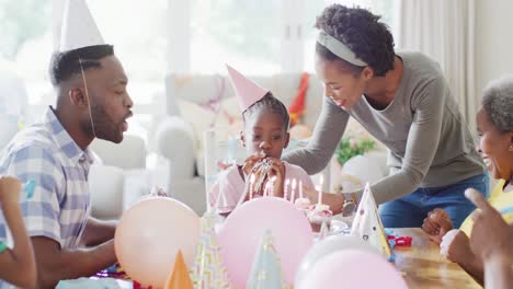 happy african american family celebrating, daughter blowing out birthday cake candles, slow motion
