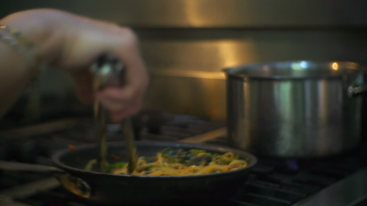 Vegetable pasta stirred and flipped in hot frying pan on kitchen stove, filmed as close up