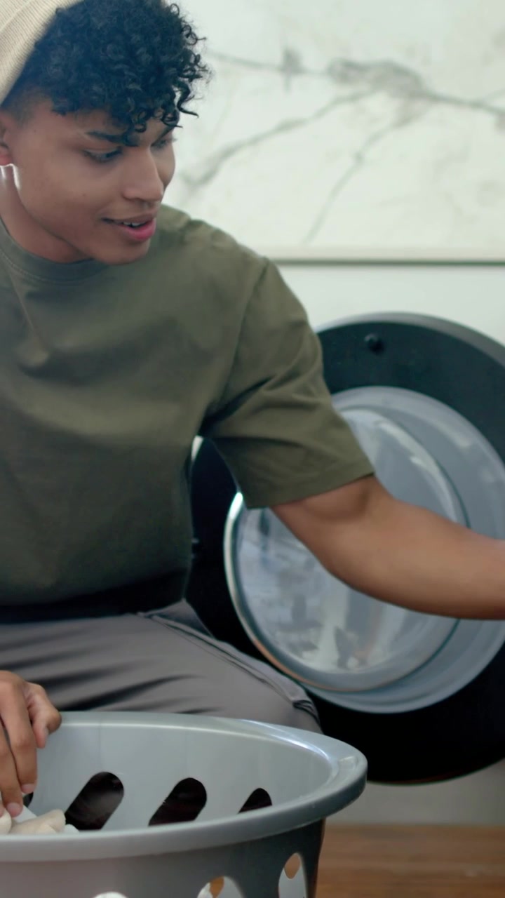 Vertical video: Seeing basket, man in beanie pulling towels from dryer at home, placing inside it