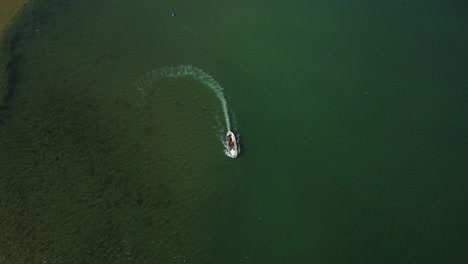 top down aerial of small fishing boat cruising on lagoon, collecting fishing nets.