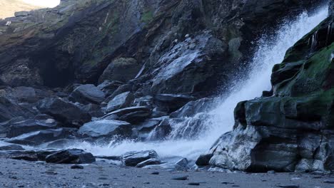 close up of waterfall flowing down cliff onto beach.