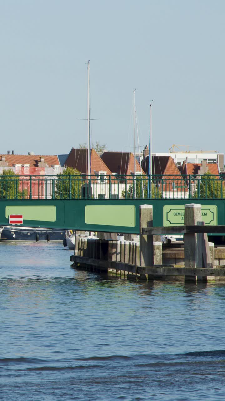 Piccole barche a motore con persone passano sotto un ponte levatoio verde, con edifici storici di una città olandese sullo sfondo.