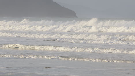 los surfistas están conquistando fuertes olas en la playa de caste point, nueva zelanda.