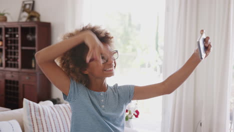 Pre-teen-girl-taking-selfies-standing-in-the-living-room-laughing,-close-up,-focus-on-foreground