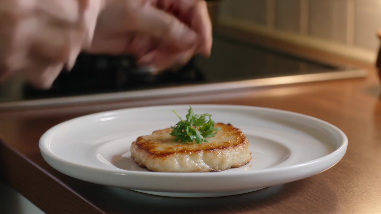 After searing cook placing microgreens on scallop at kitchen counter, sliding plate for serving