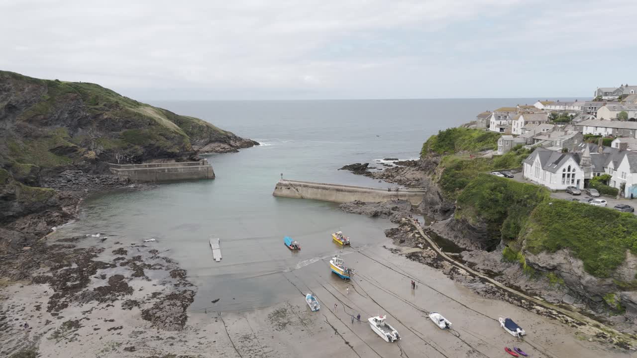 Aerial view of Port Isaac harbor with a seagull flying over boats docked along the shoreline, surrounded by cliffs and green hills, Cornwall, UK