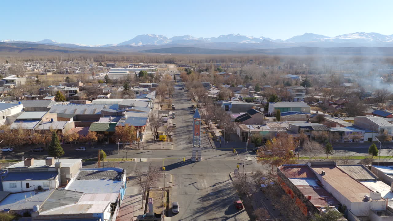 Aerial view of Avenida General Roca running through Malargüe, Mendoza, with the Andes in the distance with Winter trees and low-rise buildings frame the urban grid in this establishing drone shot.