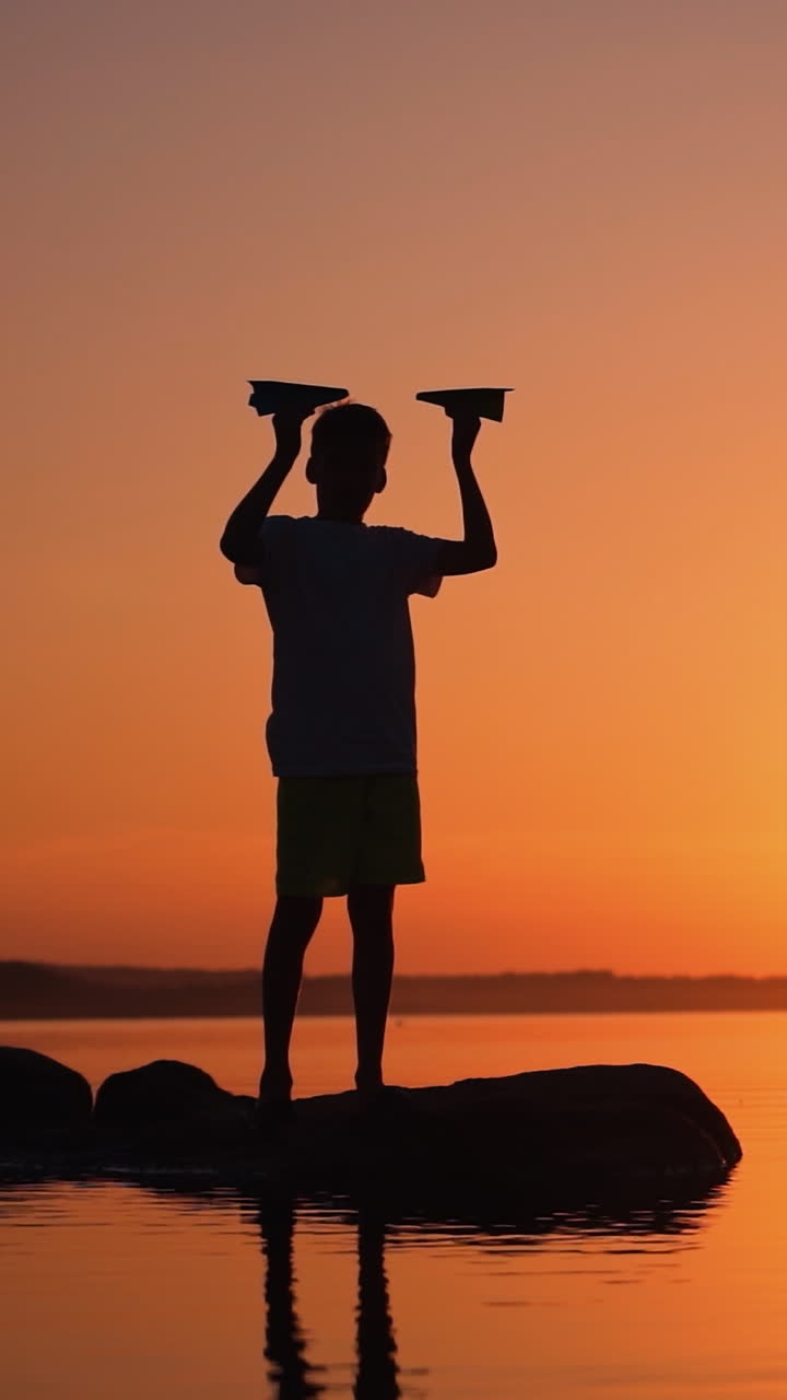 A happy child is playing with a paper airplane at sunset. Classes with children outdoors. Lifestyle Vertical video