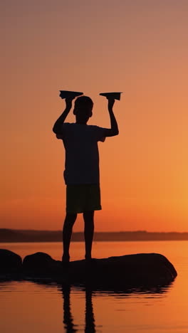 a happy child is playing with a paper airplane at sunset. classes with children outdoors. lifestyle vertical video