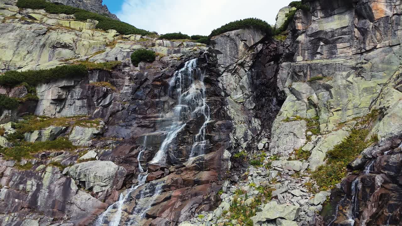 Maestosa cascata che scende a cascata lungo la parete rocciosa di una montagna con escursionisti.