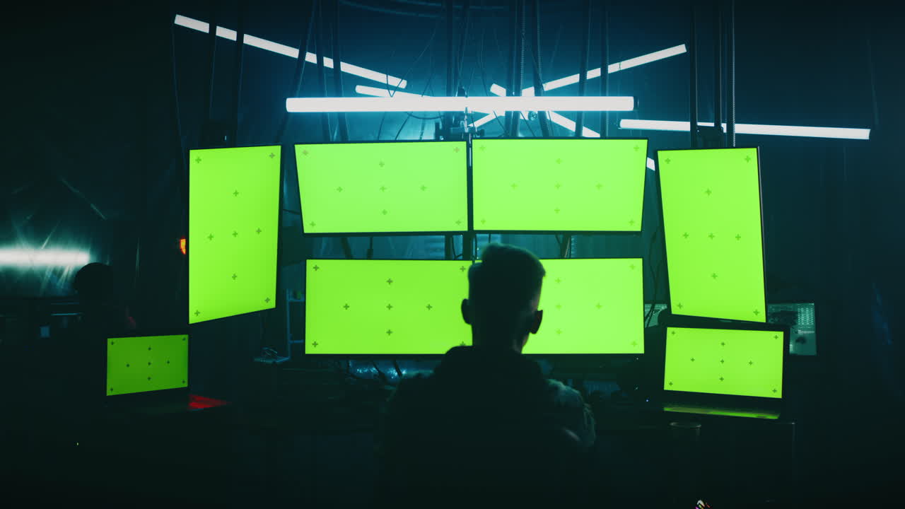 Programmer in a dark room with multiple green screen monitors