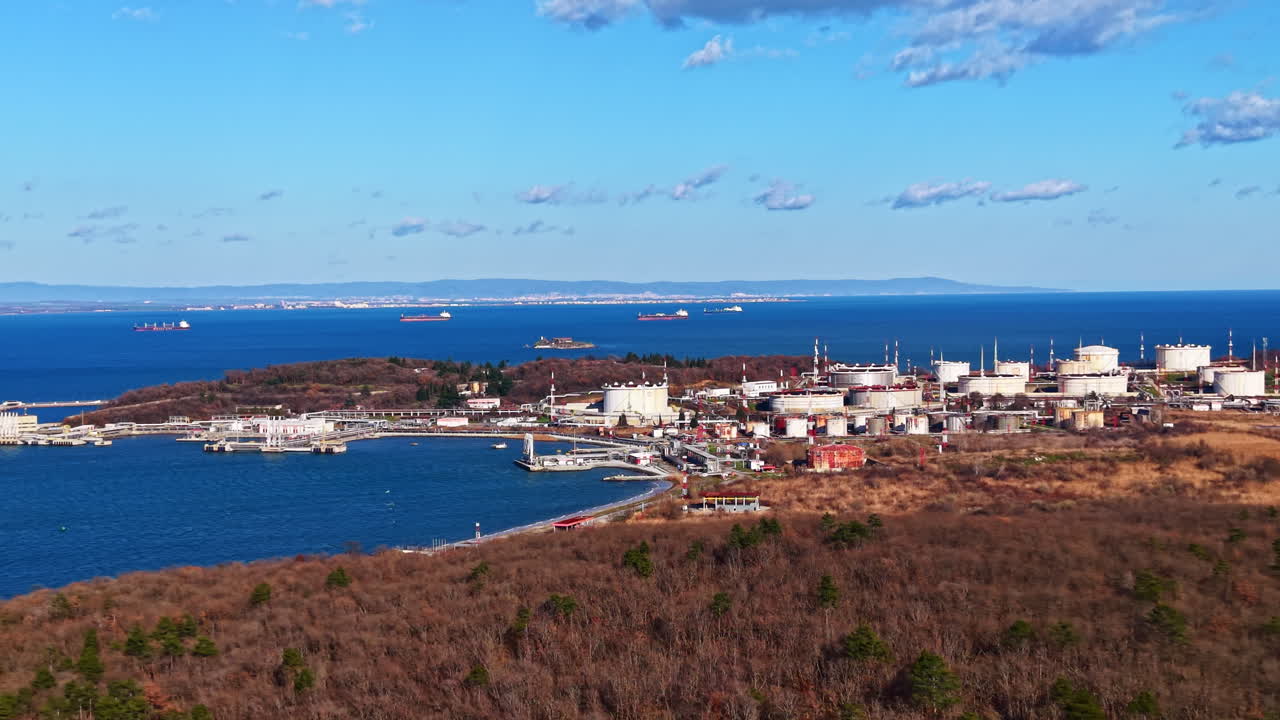 Vy över ett industriområde nära kusten med tankar och fartyg i vattnet en klar dag.