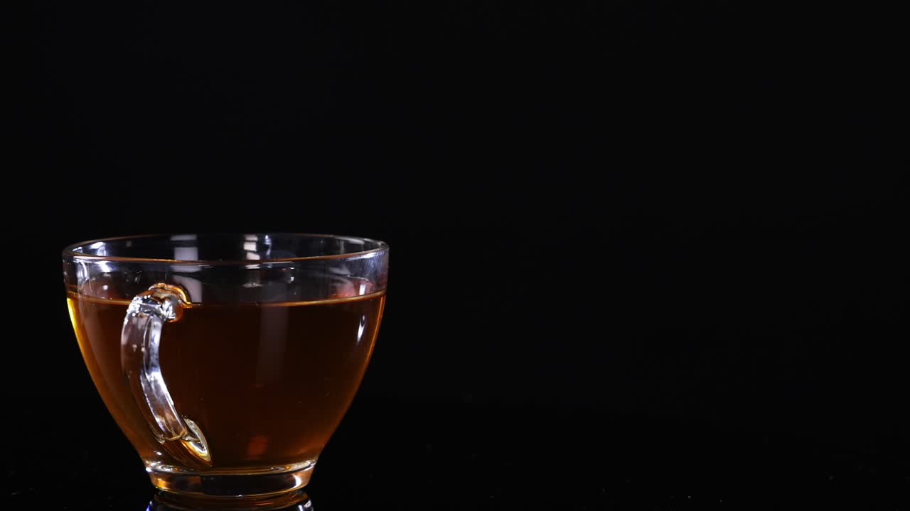 A glass cup filled with tea sits on a black background, highlighting its warm color and transparency