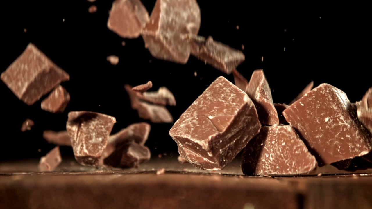 Movimento rallentato di pezzi di cioccolato che cadono su una superficie di legno scuro