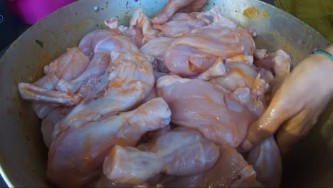 adult female hand marinating chicken pieces inside large casserole pan