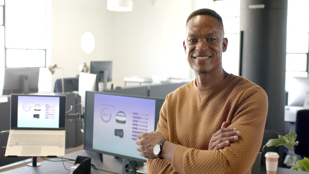 Smiling businessman standing with arms crossed in modern office with computer