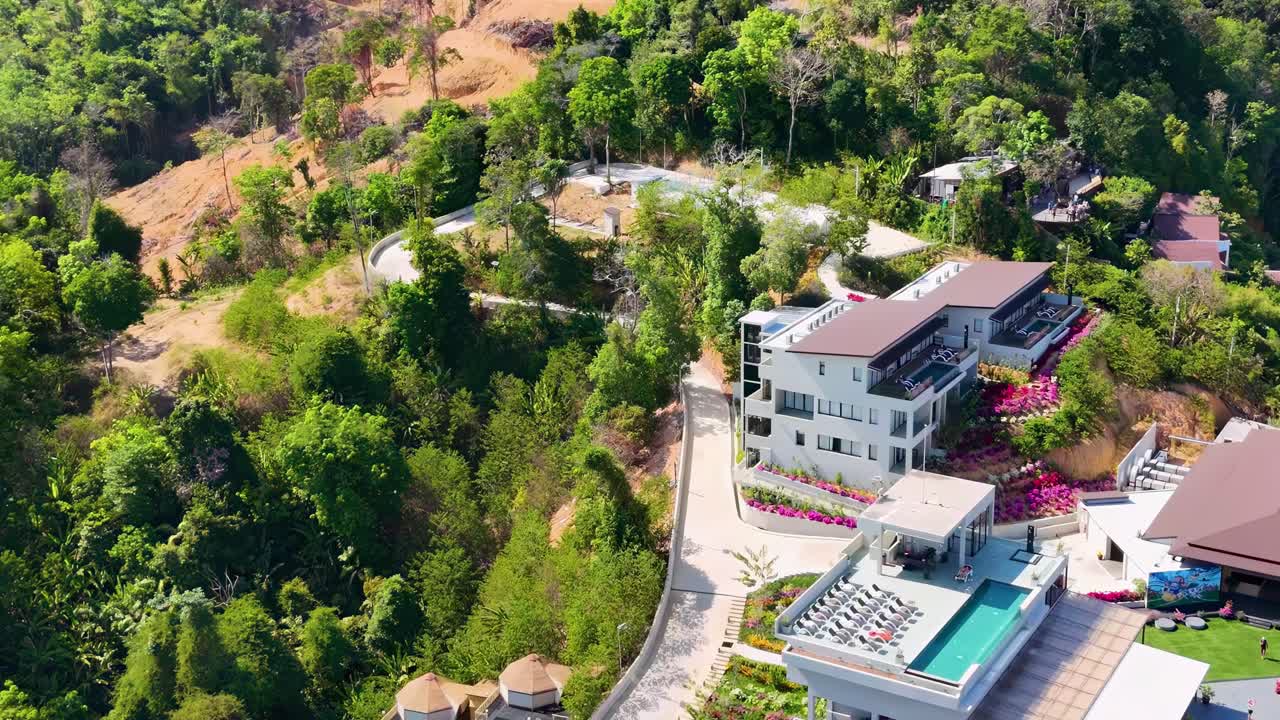 Drone captures hillside villas surrounded by dense greenery and winding paths, offering a tranquil and scenic view.