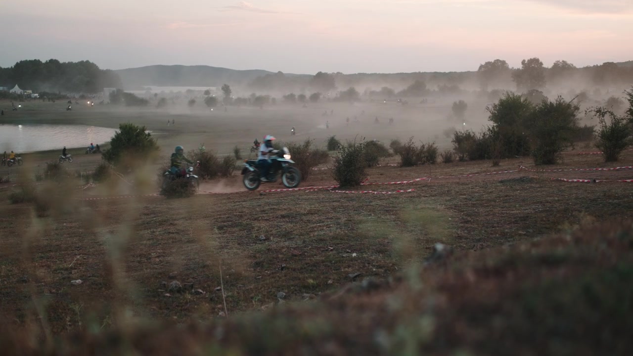 Motociclisti in fuoristrada su un campo polveroso al tramonto.