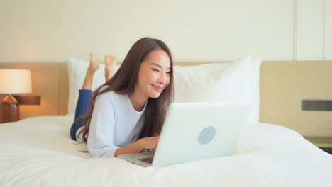 in a work from anywhere world a young woman lying on a bed inputs data into her laptop