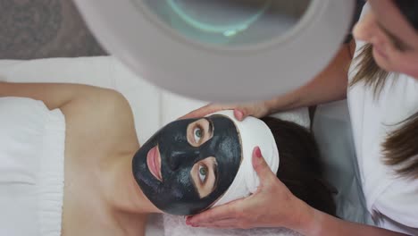 Caucasian-woman-lying-back-while-beautician-gives-her-a-face-mask