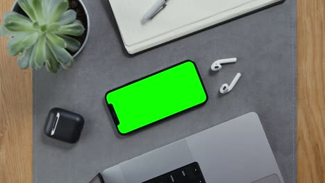 a man takes wireless headphones lying next to a smartphone with a green screen