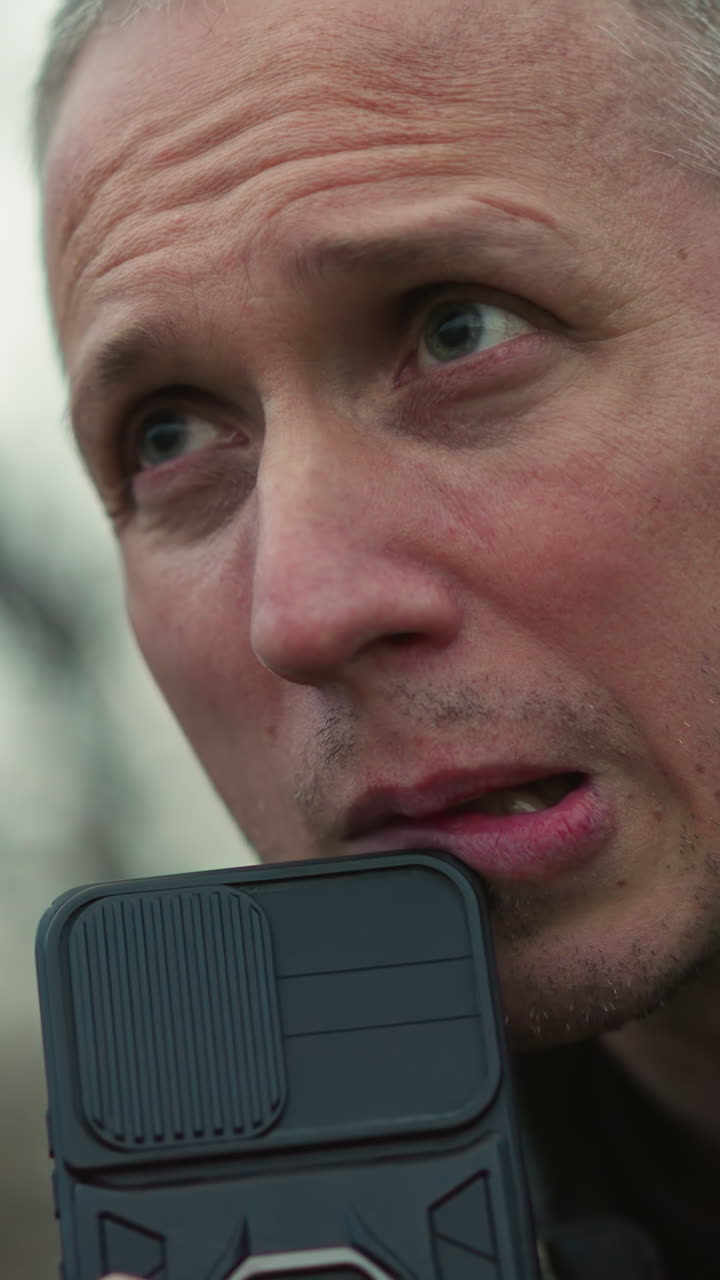 A close view of a concerned man looking intensely at something off-camera, holding a black smartphone near his mouth
