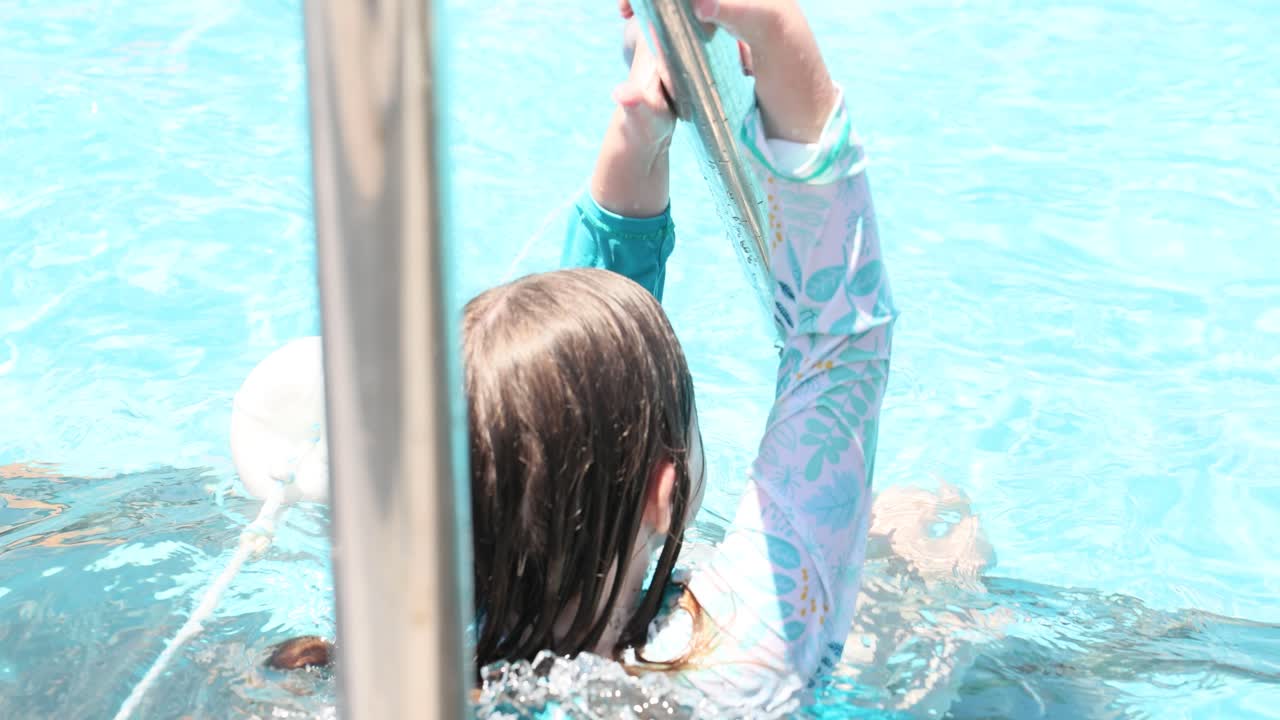 Girl in a swimming pool holding onto a ladder