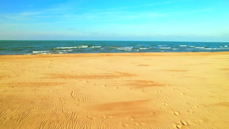 Drone-flies-over-deserted-golden-sand-beach-and-ocean-waters-with-sky-for-copy-space