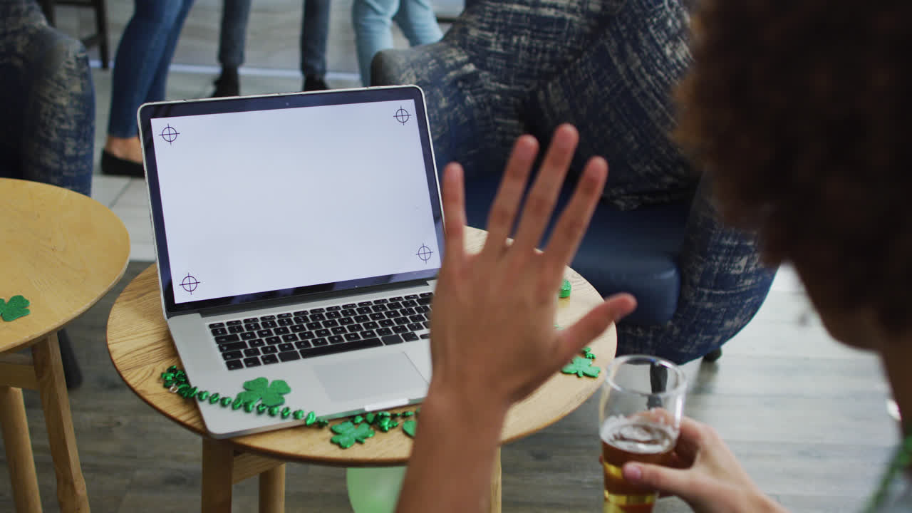 mujer de raza mixta celebrando el día de san patricio haciendo una llamada de video con una computadora portátil en un bar