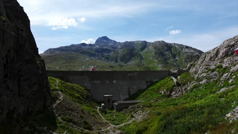 aerial view of totensee lake with its dam wall, surrounded by mountains, under a clear blue sky in switzerland. rising shot