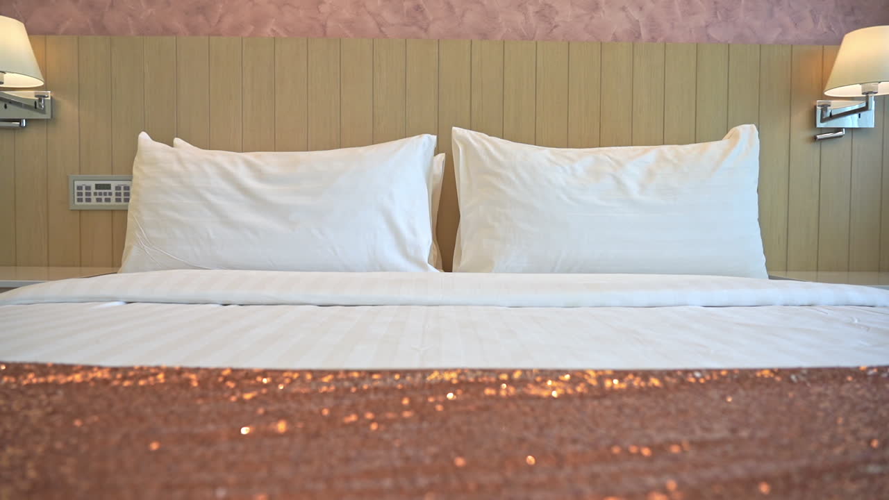 Panning shot of a clean king sized bed, inside a furnished hotel or motel bedroom