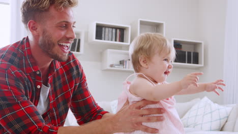 father helping daughter learn to walk at home, side view